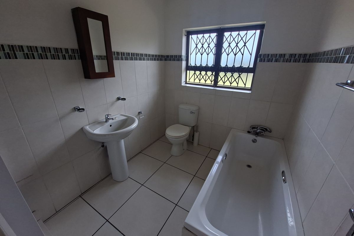 A functional bathroom featuring a pedestal basin, standard toilet, and bathtub with tiled finishes and security bars on the window.