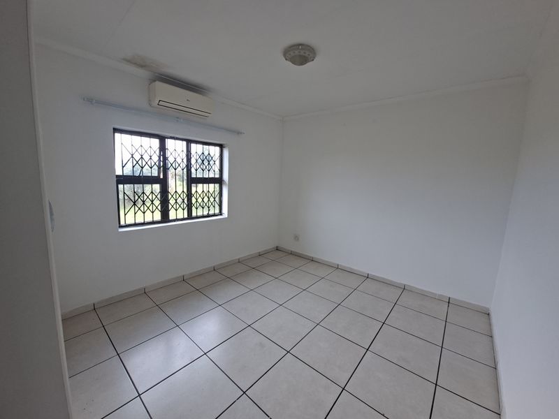 An empty bedroom featuring tiled flooring, a security gate on the window, and a wall-mounted air conditioning unit.