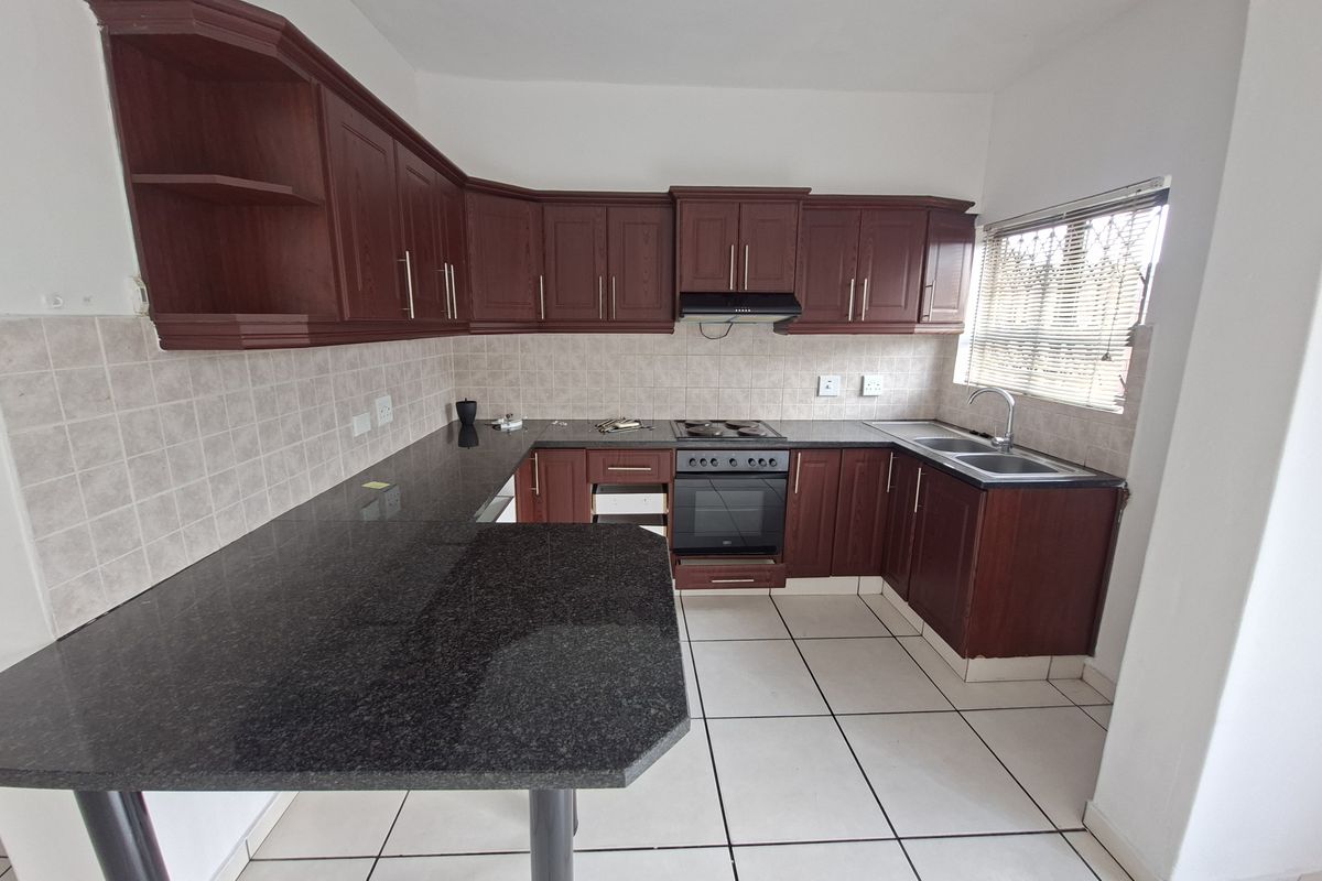 A functional kitchen featuring dark wood cabinetry, granite countertops, a built-in oven, electric hob, and a double sink with tiled backsplash.