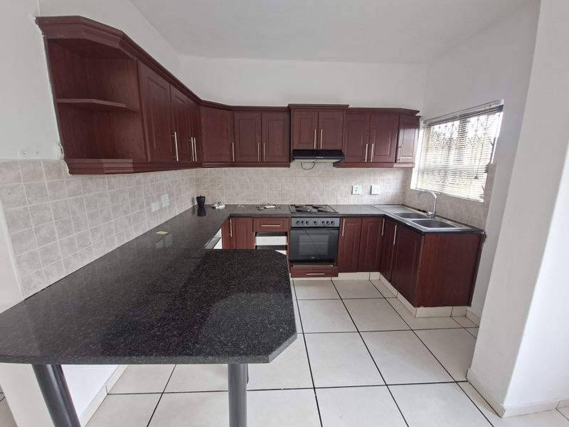 A functional kitchen featuring dark wood cabinetry, granite countertops, a built-in oven, electric hob, and a double sink with tiled backsplash.