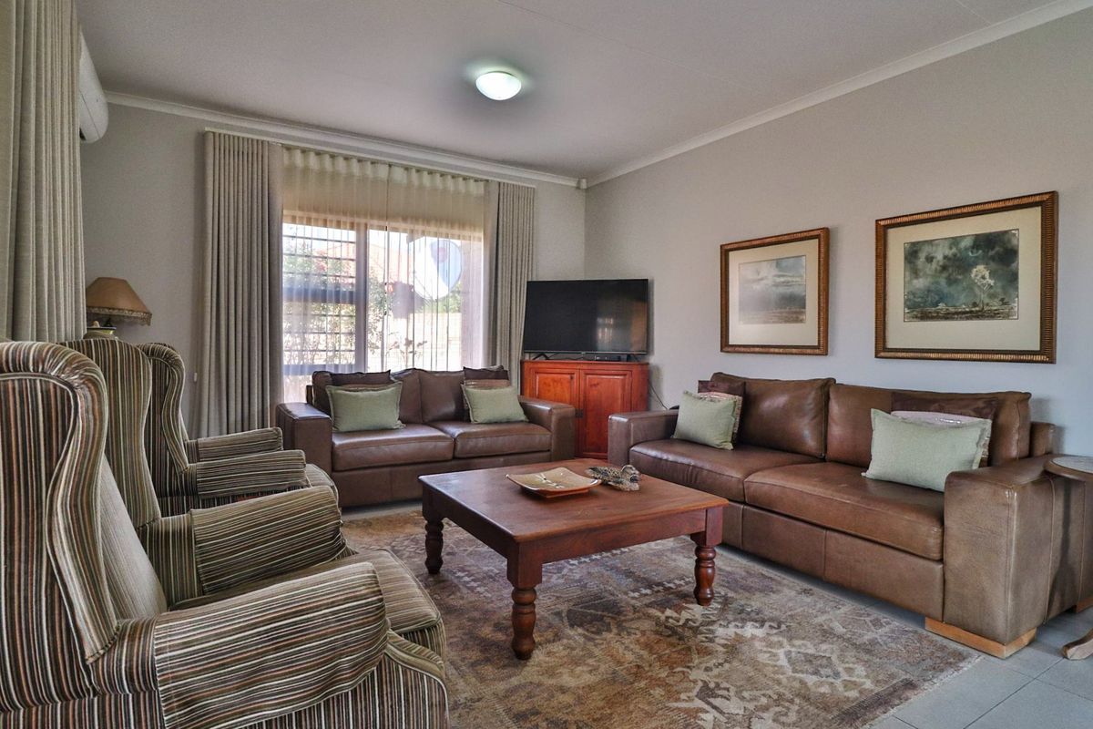 A comfortable living room featuring tiled flooring, neutral wall finishes, and large windows with curtain tracks, providing a bright and inviting space.