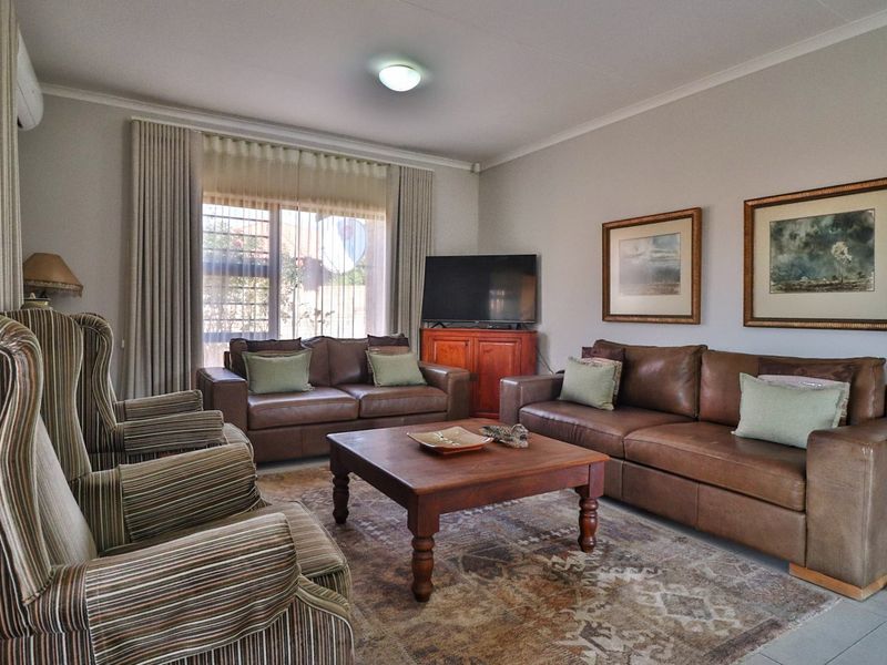 A comfortable living room featuring tiled flooring, neutral wall finishes, and large windows with curtain tracks, providing a bright and inviting space.