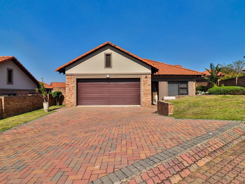 Front view of a residential property featuring a brick paved driveway, double garage, and a well-maintained front lawn with boundary walling.