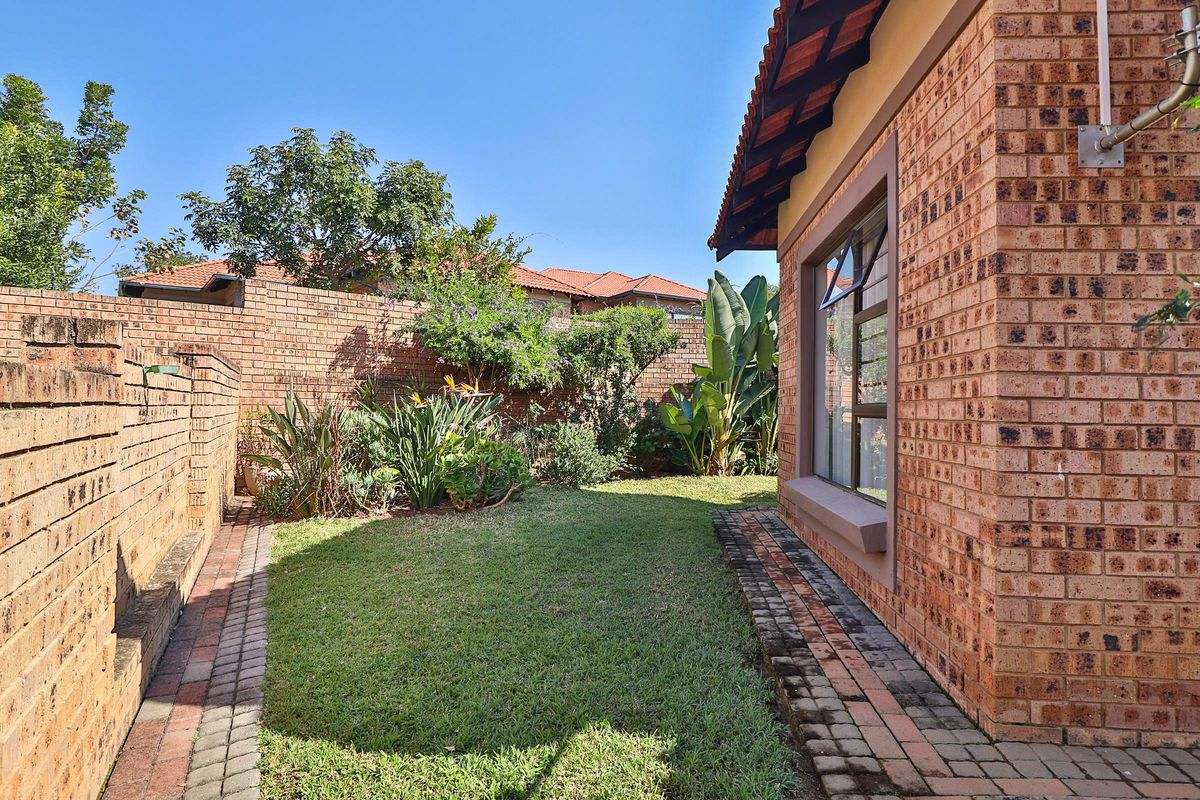 A well-maintained rear garden featuring a lawn, paved walkway, and face brick boundary walls, adjacent to the main house structure.