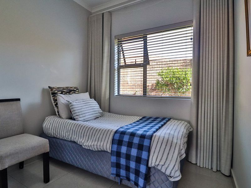 A compact, well-maintained bedroom featuring neutral tiled flooring, modern curtain tracks, and venetian blinds, providing a clean and functional living space.