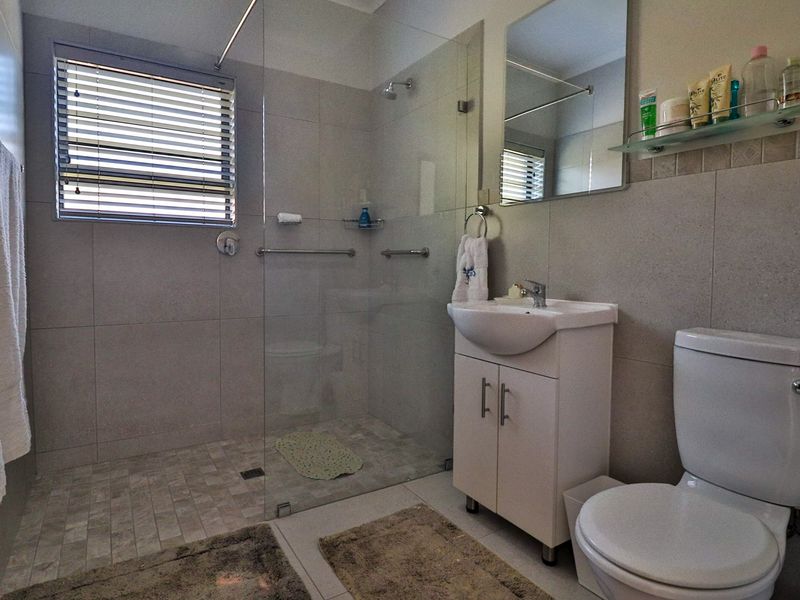 Modern bathroom featuring a walk-in shower with glass screen, vanity cabinet with basin, and neutral wall and floor tiling.