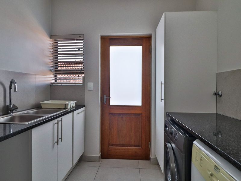 A clean and functional laundry room featuring granite countertops, built-in cabinetry, a stainless steel sink, and direct access to the exterior.