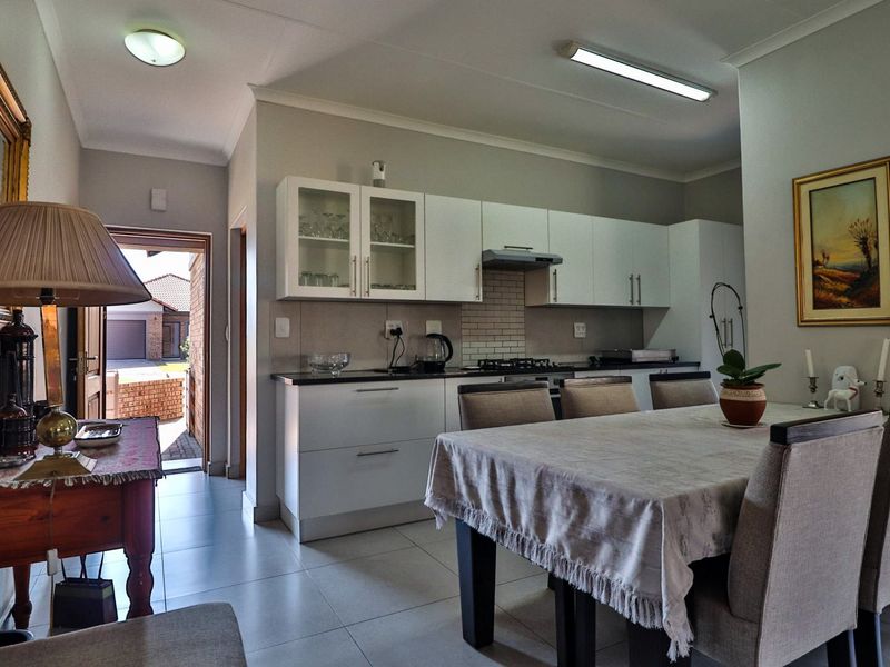 Open-plan kitchen and dining area featuring modern white cabinetry, gas hob, extractor fan, and tiled flooring with direct access to the exterior.