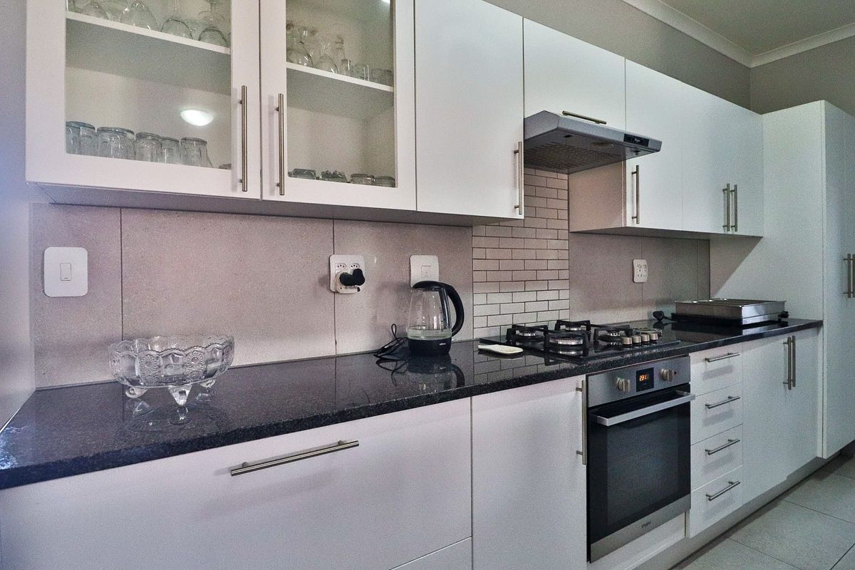 Modern kitchen featuring white cabinetry, granite countertops, subway tile backsplash, and integrated stainless steel appliances including a gas hob and oven.