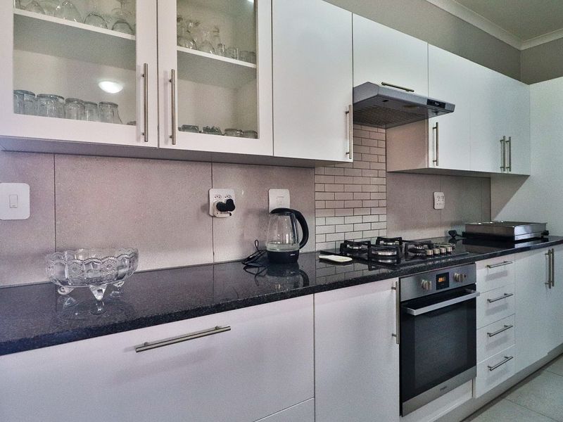 Modern kitchen featuring white cabinetry, granite countertops, subway tile backsplash, and integrated stainless steel appliances including a gas hob and oven.