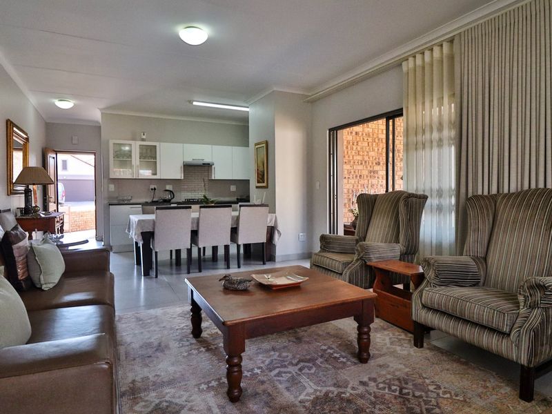 Open-plan living and dining area featuring tiled floors, neutral walls, and a functional kitchen with built-in cabinetry, leading to an outdoor patio space.