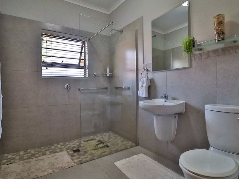 A modern, well-maintained bathroom featuring a walk-in shower with a glass screen, a pedestal basin, and neutral wall and floor tiling.