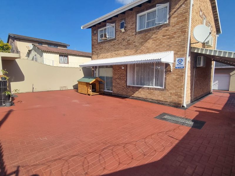 Rear view of a double-story brick house featuring a paved courtyard, protective awning, and security infrastructure.