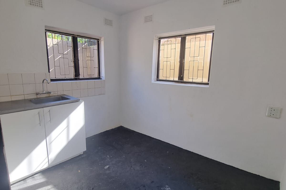 A compact, empty kitchen area featuring a single sink unit, tiled splashback, and security-barred windows, ready for renovation or custom cabinetry installation.
