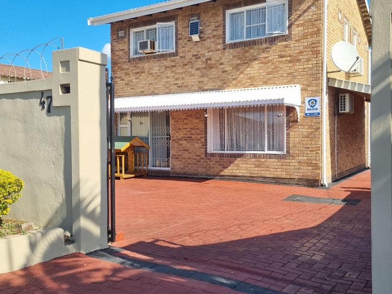 A well-maintained double-story face-brick home featuring a paved driveway, secure perimeter wall with razor wire, and an entrance awning.