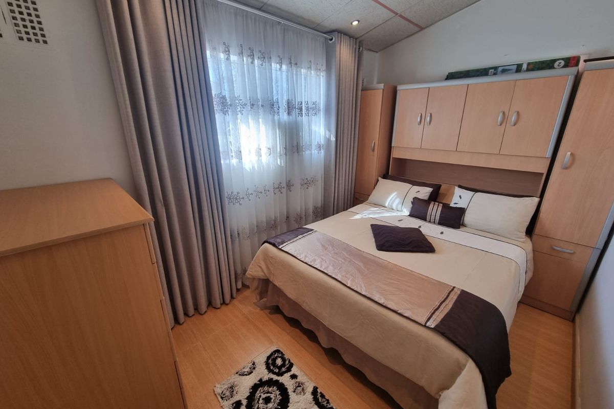 A functional bedroom featuring built-in wooden cupboards, laminate flooring, and recessed ceiling lighting, offering a practical layout for a comfortable sleeping space.