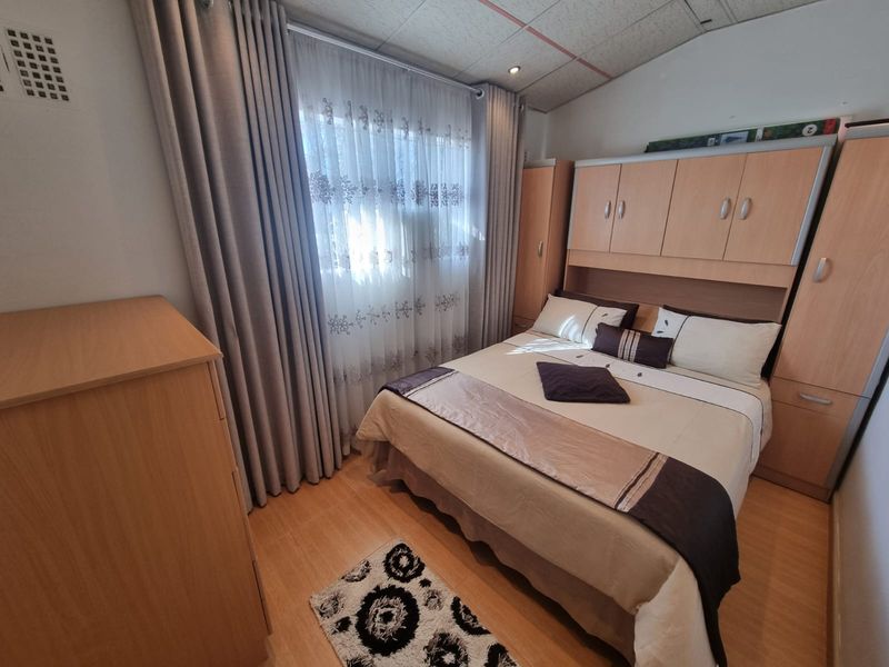 A functional bedroom featuring built-in wooden cupboards, laminate flooring, and recessed ceiling lighting, offering a practical layout for a comfortable sleeping space.