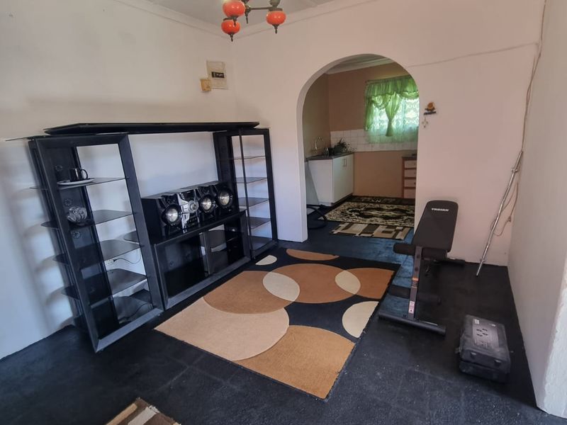 A living area featuring an arched entryway leading to a kitchen, finished with painted concrete flooring and a central chandelier.