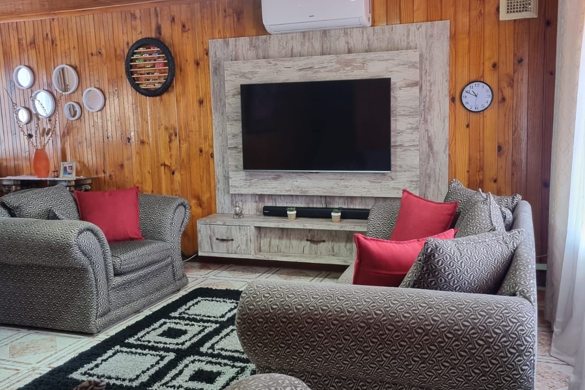 A cozy living room featuring warm timber-clad walls and ceilings, tiled flooring, and a built-in media unit with an integrated air conditioning system.