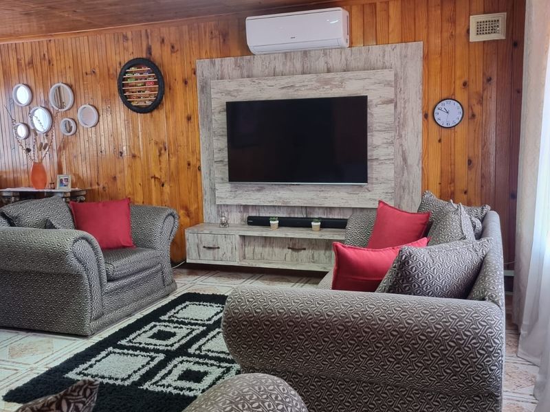 A cozy living room featuring warm timber-clad walls and ceilings, tiled flooring, and a built-in media unit with an integrated air conditioning system.
