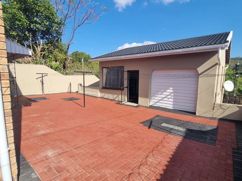 A well-maintained rear exterior area featuring red brick paving, a single garage, and secure window bars under a clear blue sky.