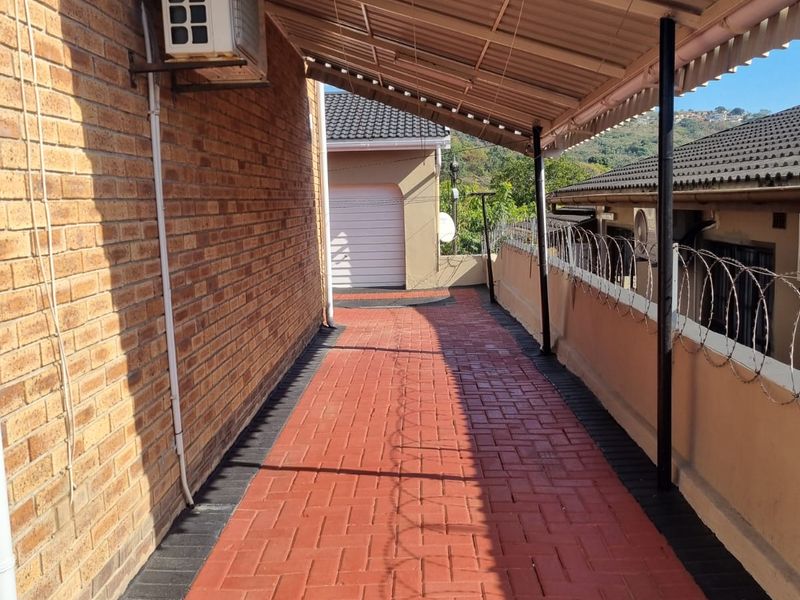 A covered outdoor walkway featuring red brick paving, a corrugated metal roof, and secure perimeter fencing with razor wire.
