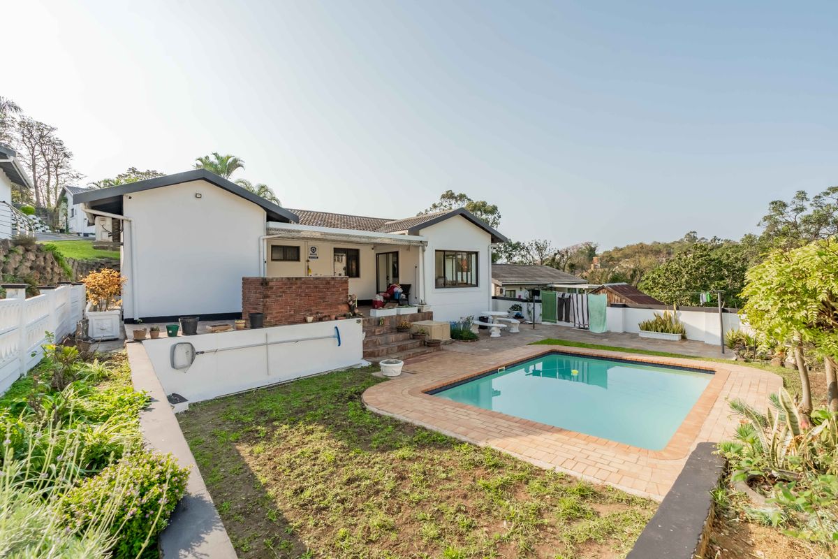 Rear exterior view of the townhouse featuring a swimming pool, paved patio area, and a built-in brick braai, set within a private garden space.