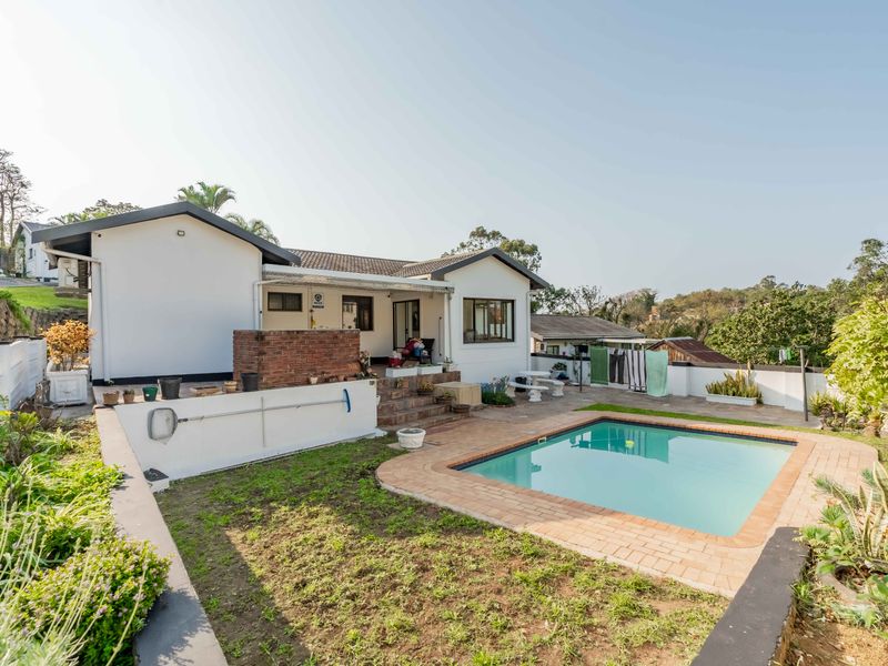 Rear exterior view of the townhouse featuring a swimming pool, paved patio area, and a built-in brick braai, set within a private garden space.