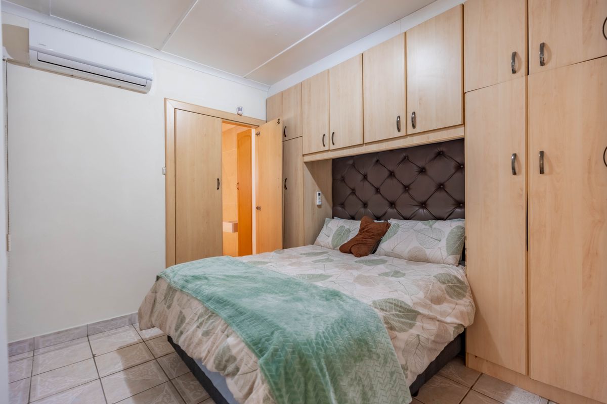 Bedroom featuring built-in light wood cabinetry, tiled flooring, and a wall-mounted split-system air conditioner, with an adjoining en-suite bathroom.
