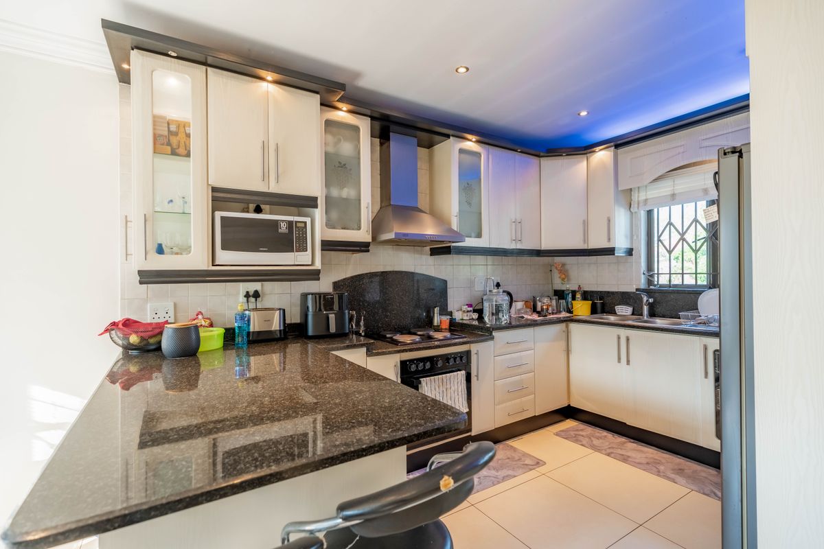 A well-maintained kitchen featuring granite countertops, ample built-in cabinetry, integrated appliances, and tiled flooring with recessed lighting.