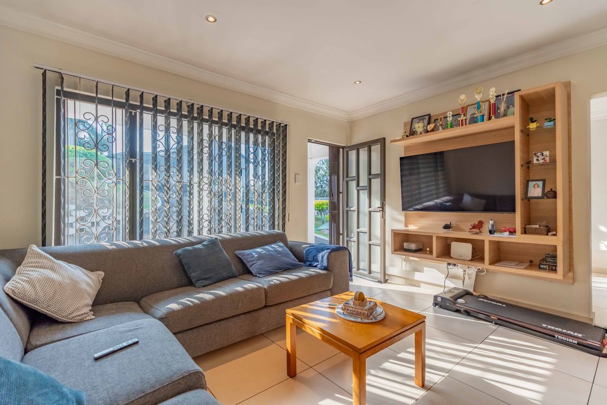 A bright living room featuring tiled flooring, recessed downlights, and a custom built-in wooden shelving unit with direct access to an outdoor area.