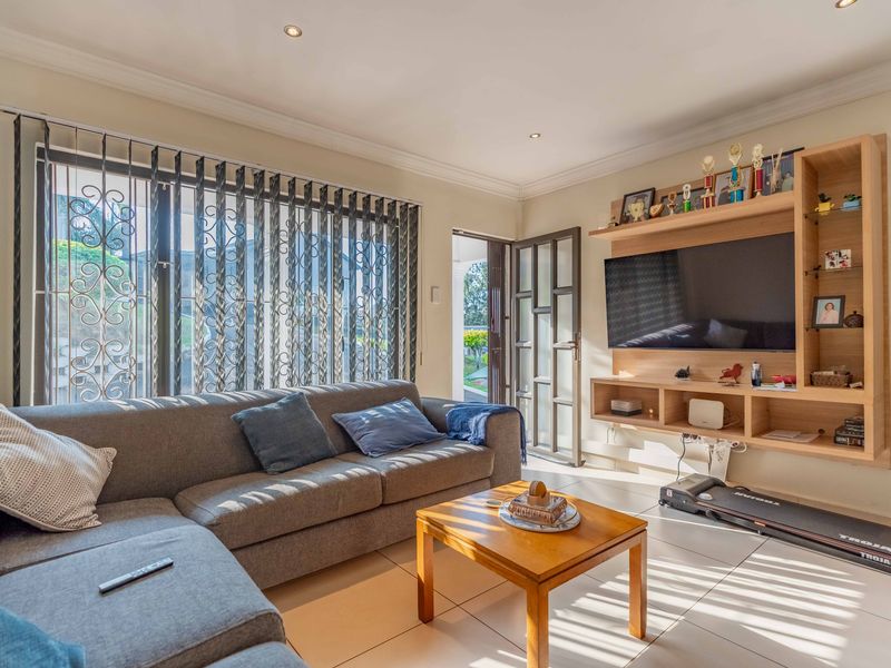 A bright living room featuring tiled flooring, recessed downlights, and a custom built-in wooden shelving unit with direct access to an outdoor area.