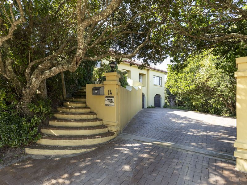 Front entrance view featuring a brick paved driveway, masonry boundary wall, and concrete stairs leading to the property entrance.