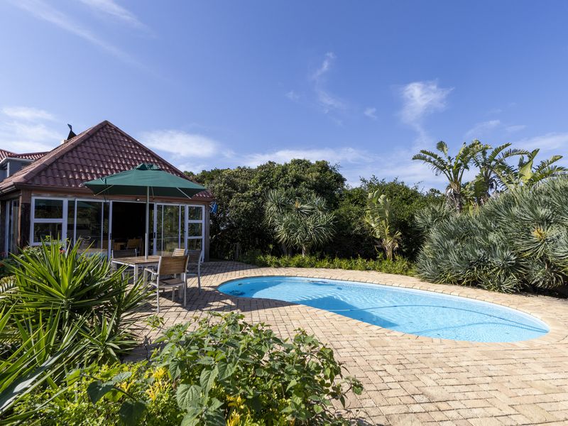 A well-maintained outdoor pool area featuring a paved patio, landscaped garden, and direct access to the home through sliding glass doors.