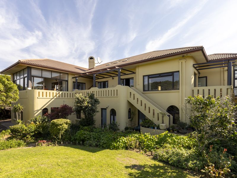 Rear view of a multi-level residence featuring a stucco facade, terracotta roof, elevated balcony with pergola, and an external staircase leading to the garden.