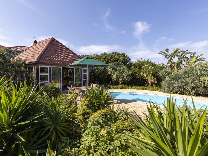 A well-maintained outdoor pool area featuring a brick-paved deck, a charming gazebo with a tiled roof, and lush surrounding garden landscaping.