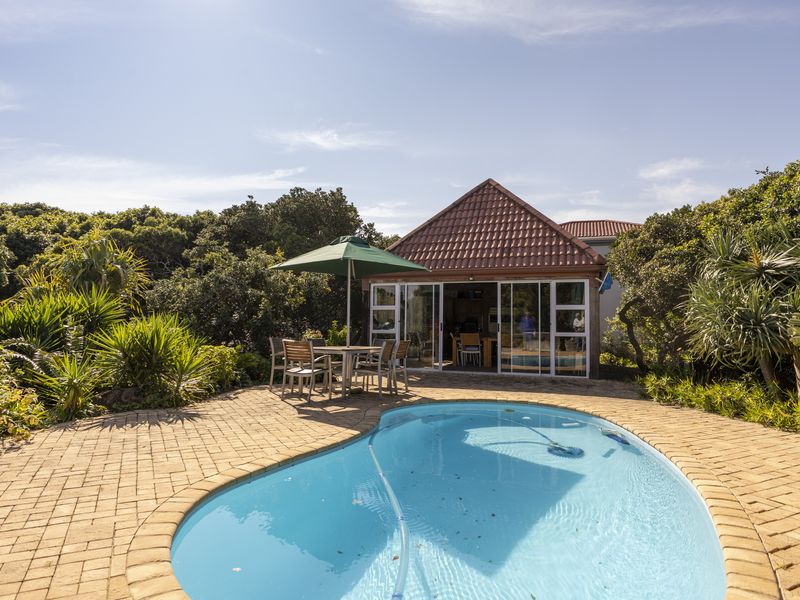 A well-maintained outdoor pool area featuring a paved deck, landscaped garden surroundings, and direct access to the home through sliding glass doors.