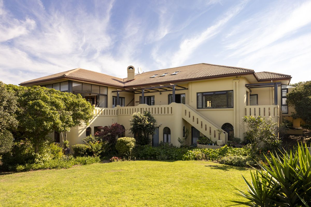 Rear view of a multi-level residence featuring a tiled roof, balcony with external staircase, pergola, and landscaped garden.