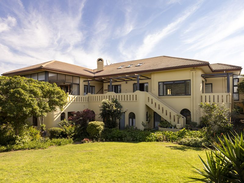 Rear view of a multi-level residence featuring a tiled roof, balcony with external staircase, pergola, and landscaped garden.