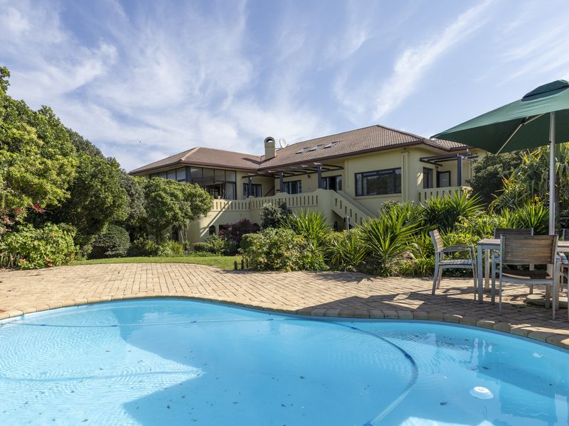 A well-maintained rear garden featuring a swimming pool, paved deck area, and a spacious two-story house with a tiled roof and balcony.