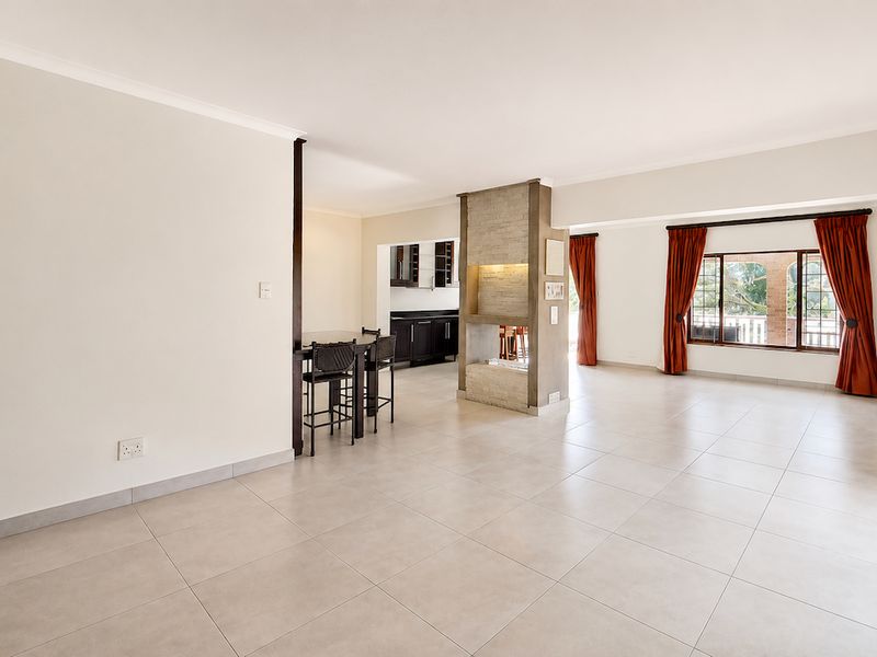 Spacious open-plan living and dining area featuring neutral tiled flooring, a central stone-clad fireplace, and a connected kitchen space.