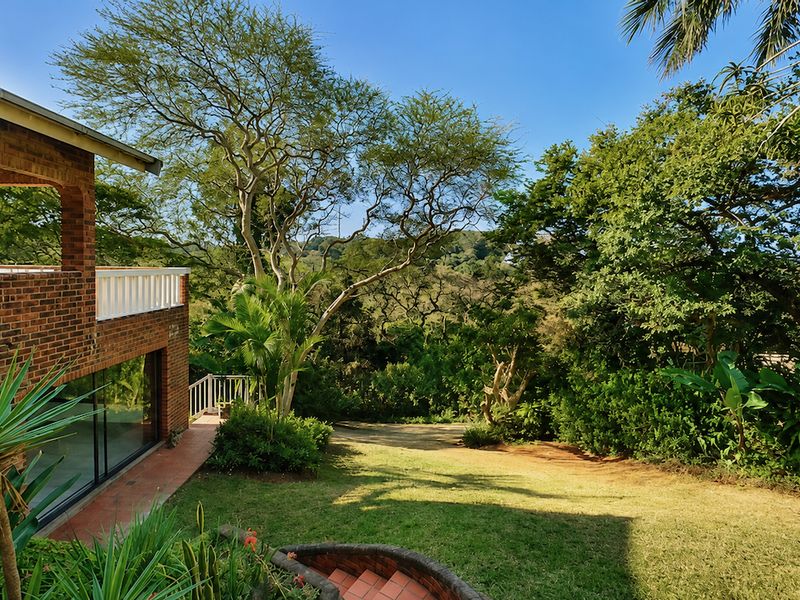 Rear view of a brick house featuring a covered patio, sliding glass doors, and a landscaped garden overlooking a natural wooded area.