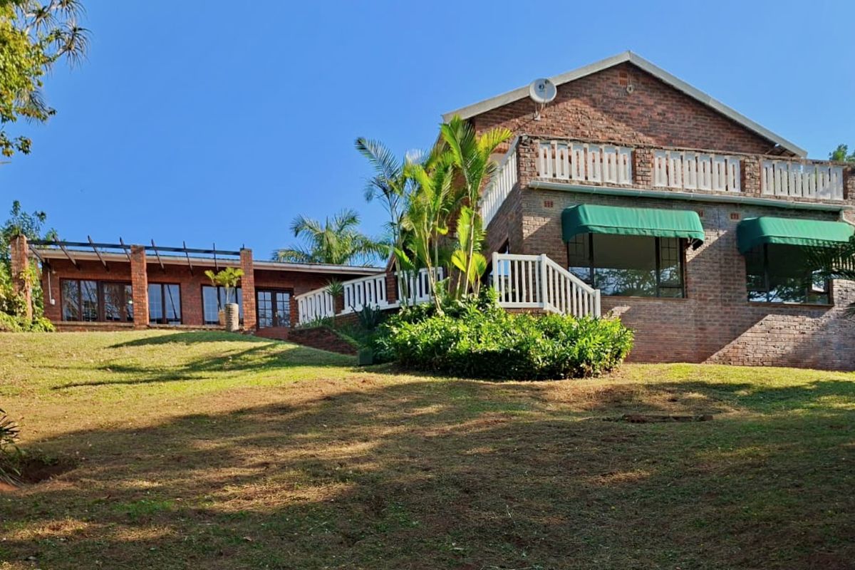 Rear view of a multi-level brick house featuring a balcony, outdoor terrace area, and established garden surroundings.