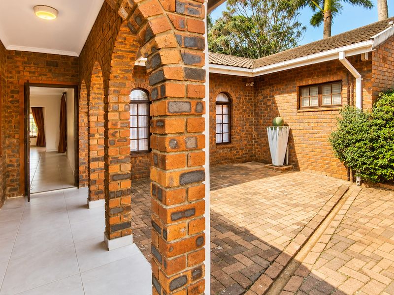 A spacious covered patio featuring classic brick arches, paved flooring, and direct access to the home's interior through a secure entrance.