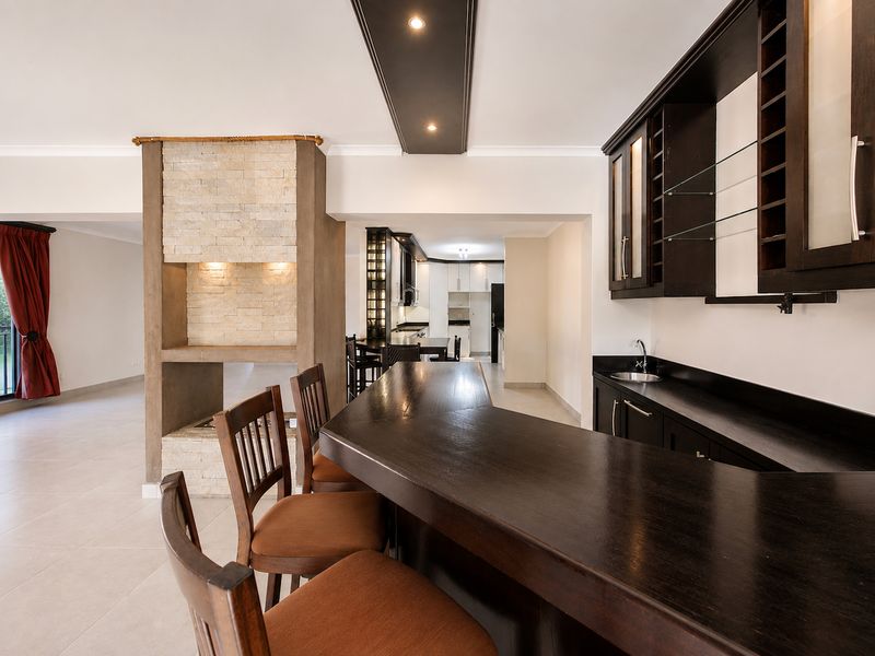Open-plan living area featuring a built-in bar, stone-clad fireplace, and modern cabinetry, seamlessly connecting to the kitchen space.