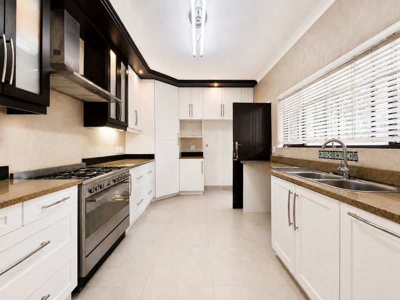 Modern kitchen featuring white cabinetry, dark contrasting accents, stone countertops, a gas hob with extractor, and tiled flooring in a clean, functional layout.