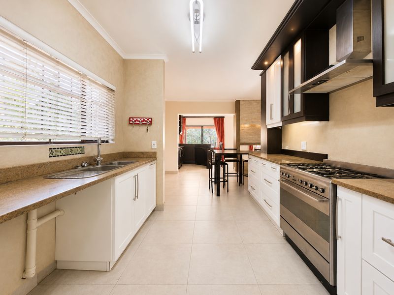 A well-maintained kitchen featuring granite countertops, stainless steel gas stove, extractor fan, and ample built-in cabinetry with a clean, functional layout.