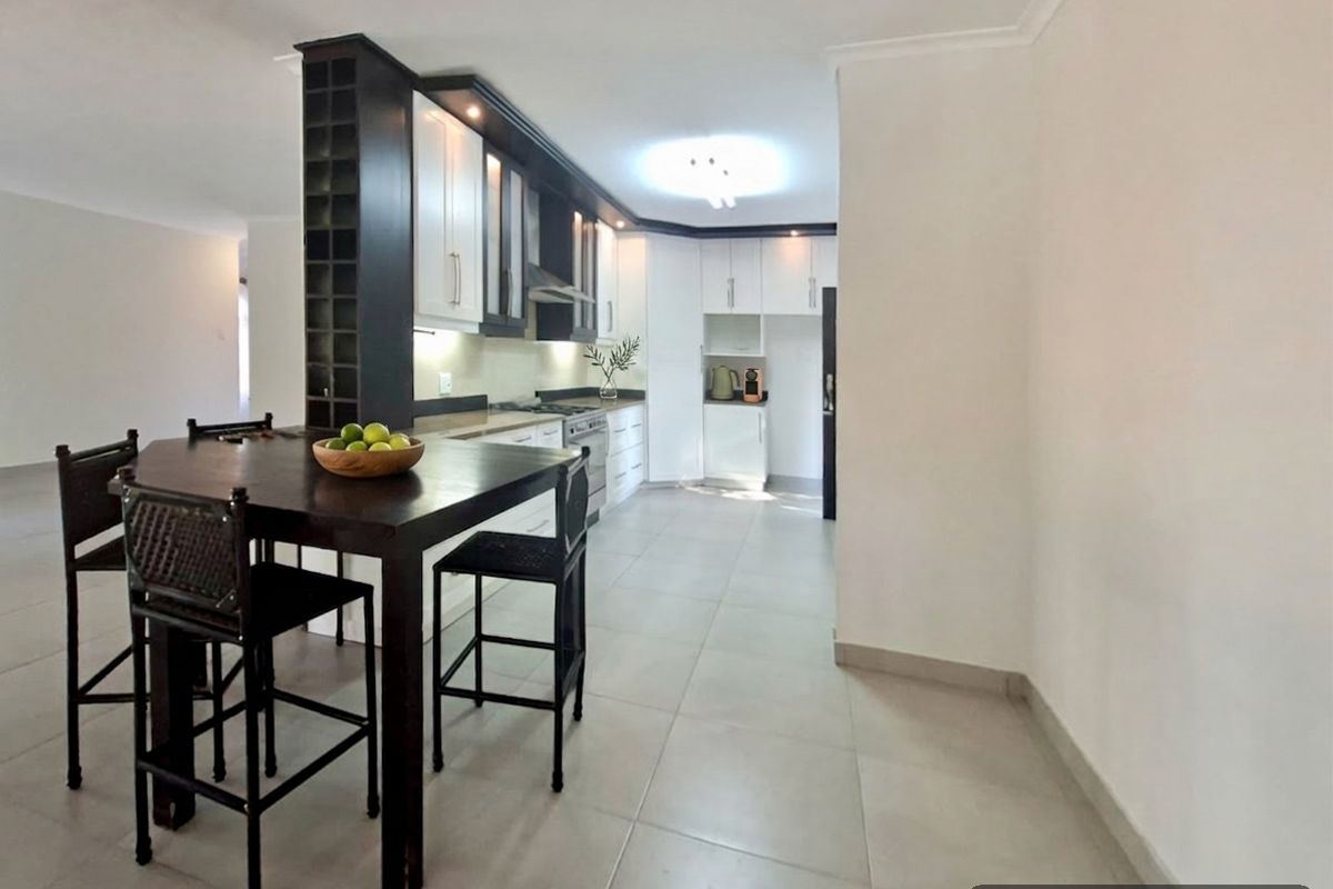 Modern kitchen featuring white cabinetry, dark accents, built-in appliances, and tiled flooring, seamlessly integrated with a dining area.