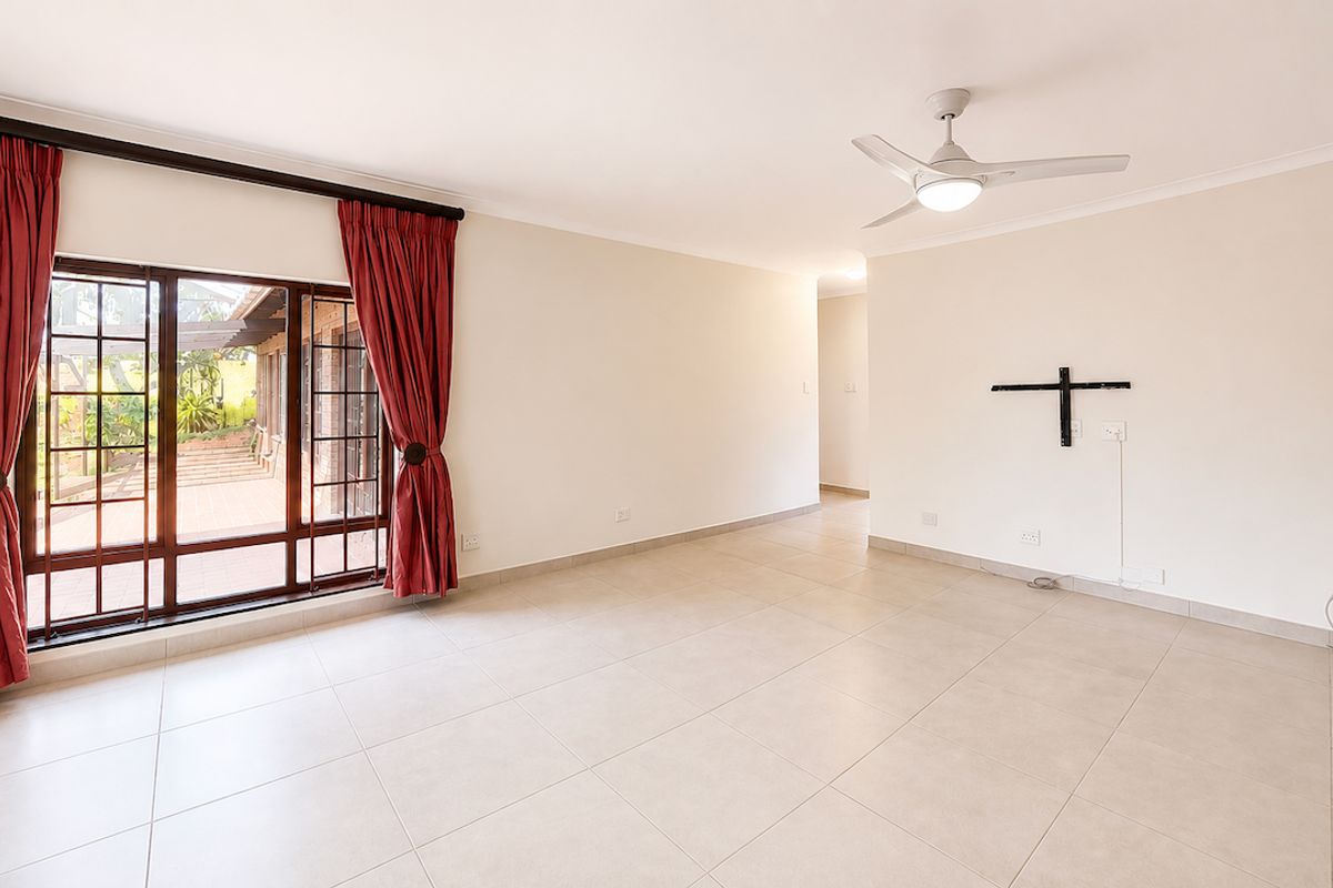 A bright, spacious, and empty living room featuring neutral tiled flooring, a ceiling fan, and large sliding glass doors leading to an outdoor patio area.