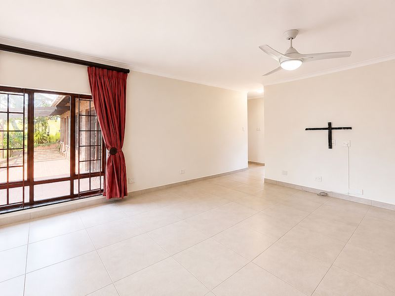 A bright, spacious, and empty living room featuring neutral tiled flooring, a ceiling fan, and large sliding glass doors leading to an outdoor patio area.
